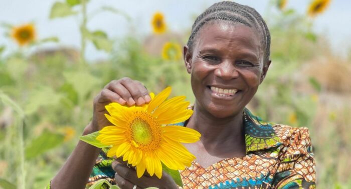 Anicia Samwel håller i en solros på ett blommande solrosfält i Tanzania i strålande sol.